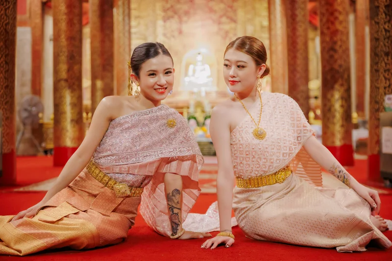 Two women in Thai sabai costumes at temple interior — friends photoshoot